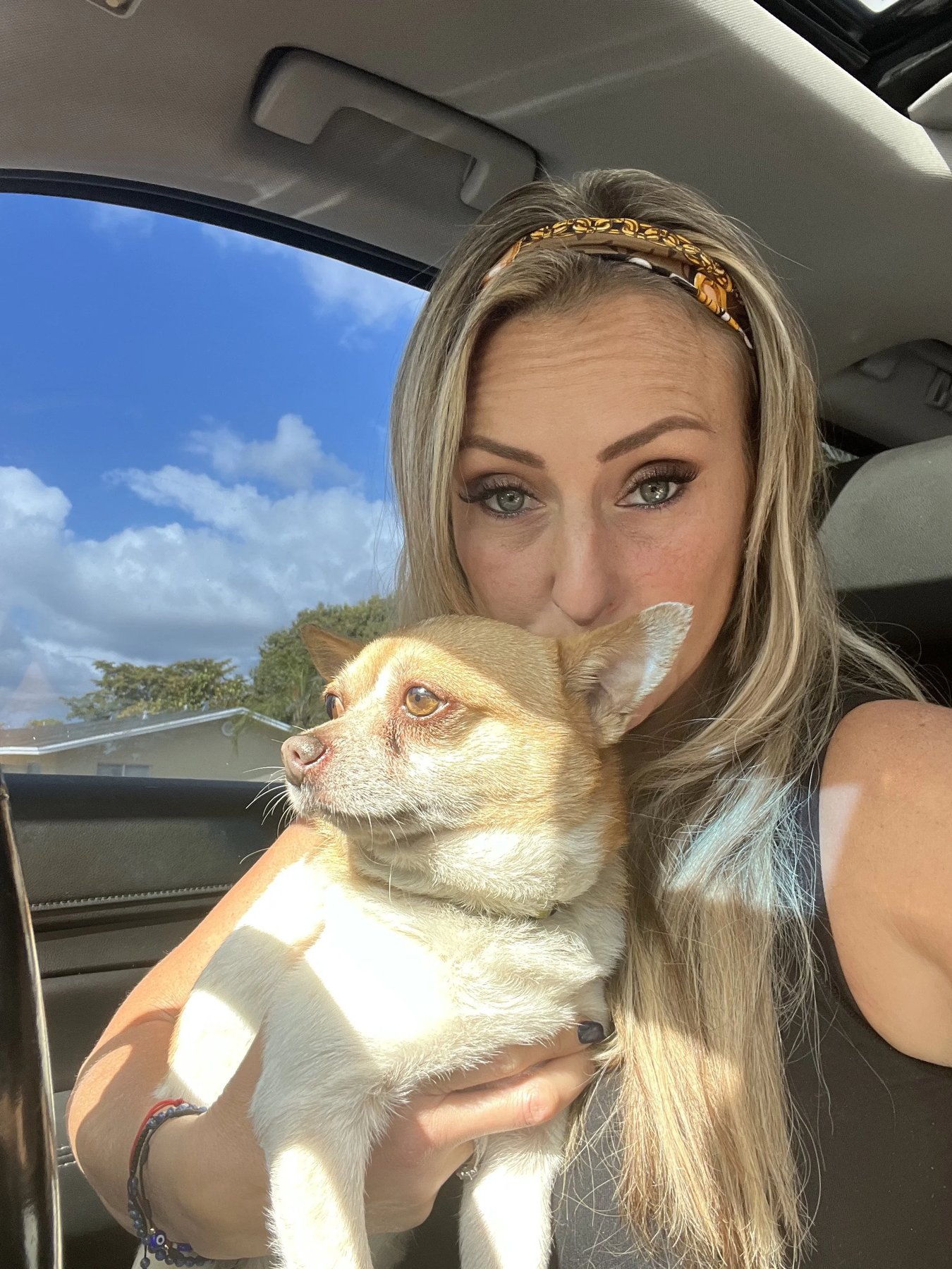Tiffany Skuraton, founder of Blue Waters Dog Rescue, in a car holding a small tan-and-white Chihuahua mix close to her face